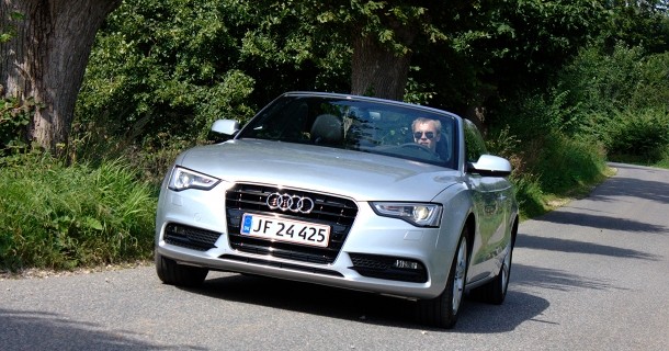 Hvid Audi A5 cabriolet med åbent tag kører på landevej omgivet af grønt træ