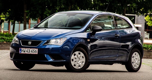 Blå Suzuki Swift hatchback parkeret på vej med grønt område i baggrund