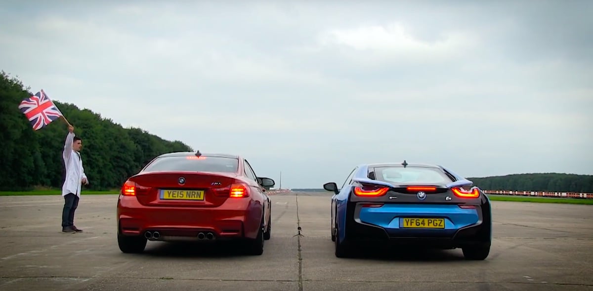 Rød BMW M4 og blå BMW i8 parkeret på flypladsbane med person der holder britisk flag