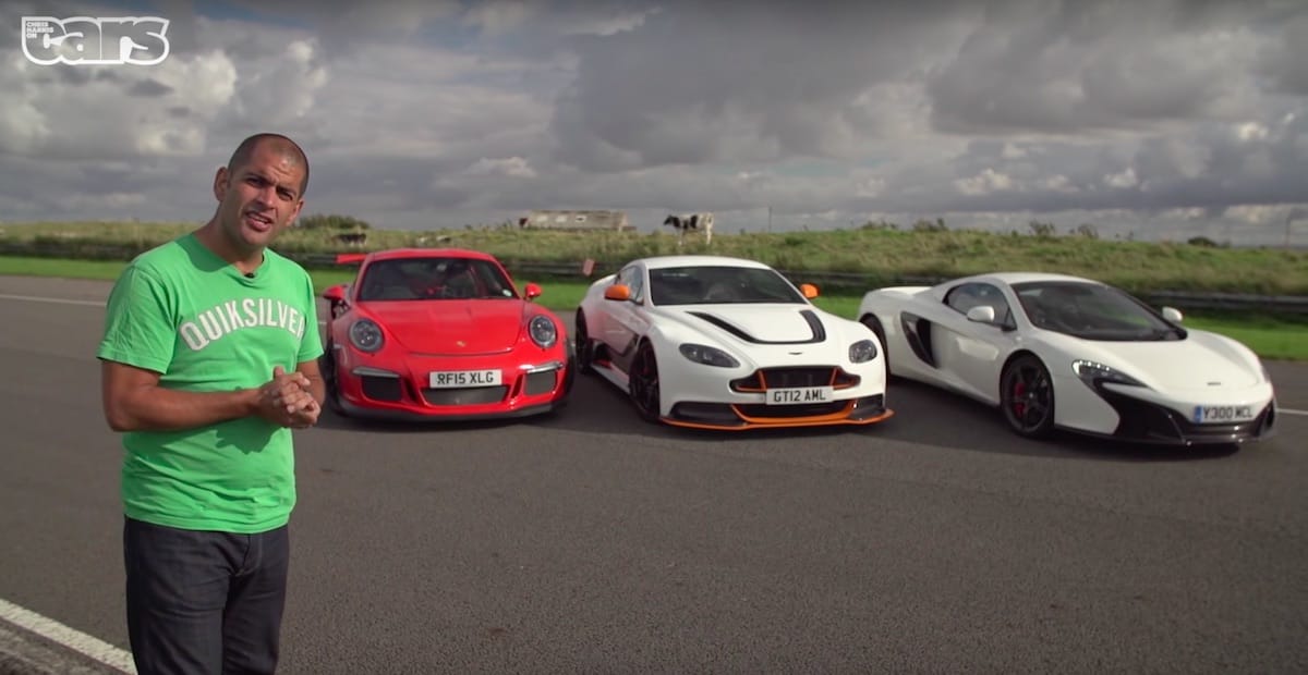 Mand i grøn t-shirt foran tre sportsvogne: rød Porsche, hvid Aston Martin og hvid McLaren på åben vejbane