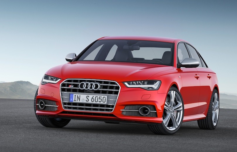 Rød Audi S6 firehjulet sedan fotograferet forfra på asfalt med bjerge i baggrunden