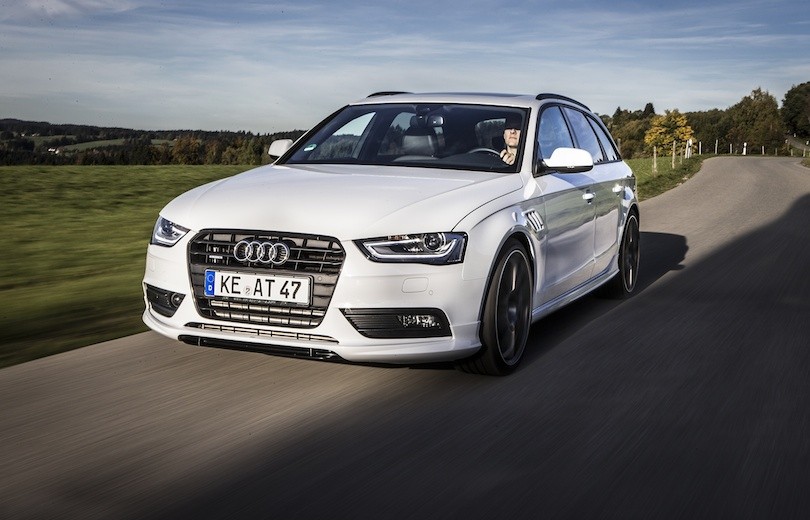 Hvid Audi A4 Allroad kører på asfaltvej med grønne marker og træer i baggrunden