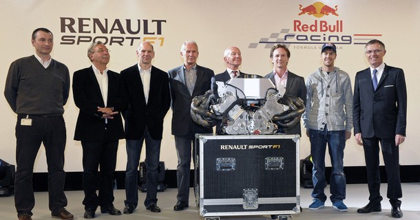 Gruppe af personer i formelt tøj står foran Renault Sport og Red Bull banner med racingudstyr på podium
