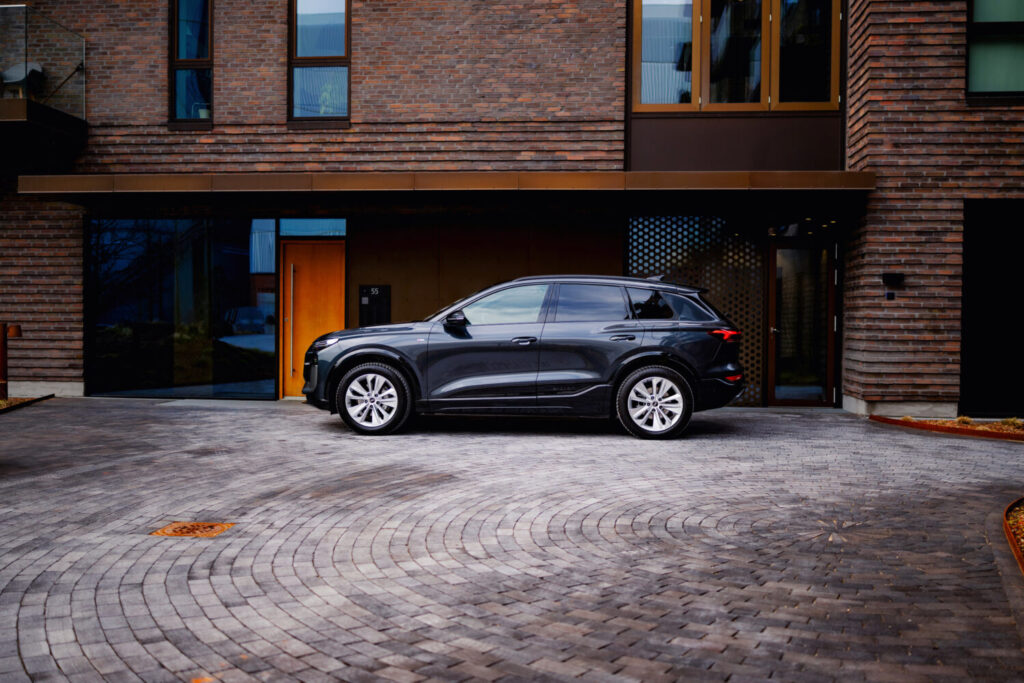 En mørk Audi SUV set fra siden holder parkeret foran en moderne bygning med murstensfacade og store vinduer. Den rolige, urbane scene fremhæver bilens elegante linjer og passer naturligt til Bilsektionen og Audi.