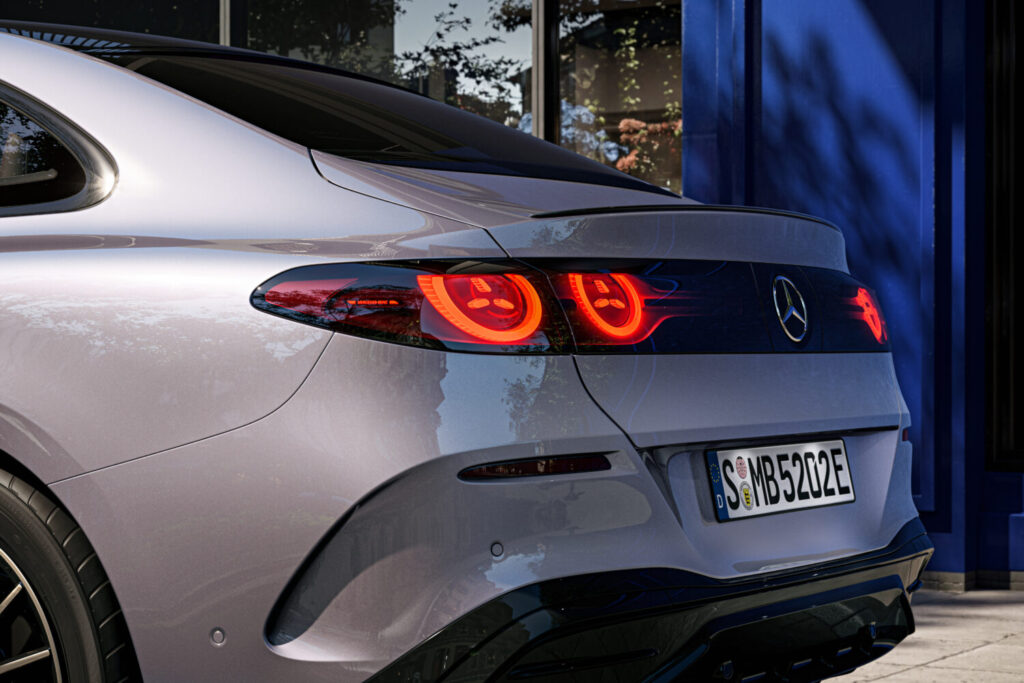 Nærbillede af bagenden på en sølvgrå Mercedes med oplyste røde baglygter og logo centralt placeret. Detaljen fremhæver design og finish i en urban setting der passer til Bilsektionen og Mercedes.