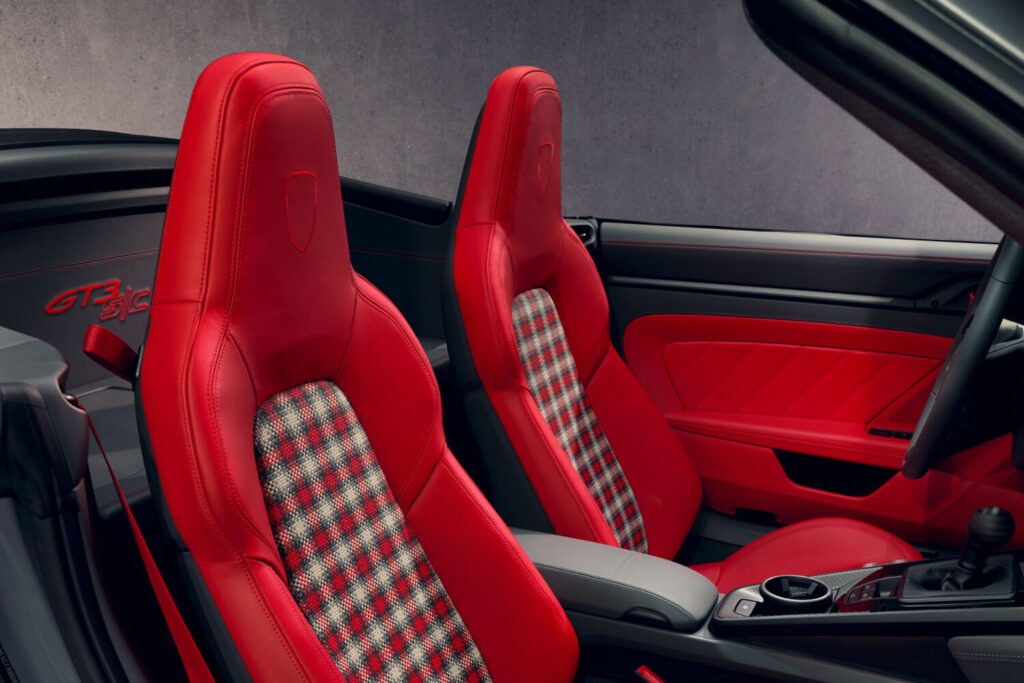 Interiør af en Porsche med to røde sportssæder i læder og ternet stofindlæg samt “GT3 RS” tekst synlig bag sæderne. Detaljen fremhæver luksus og sporty design i en kabine der passer til Bilsektionen og Porsche.