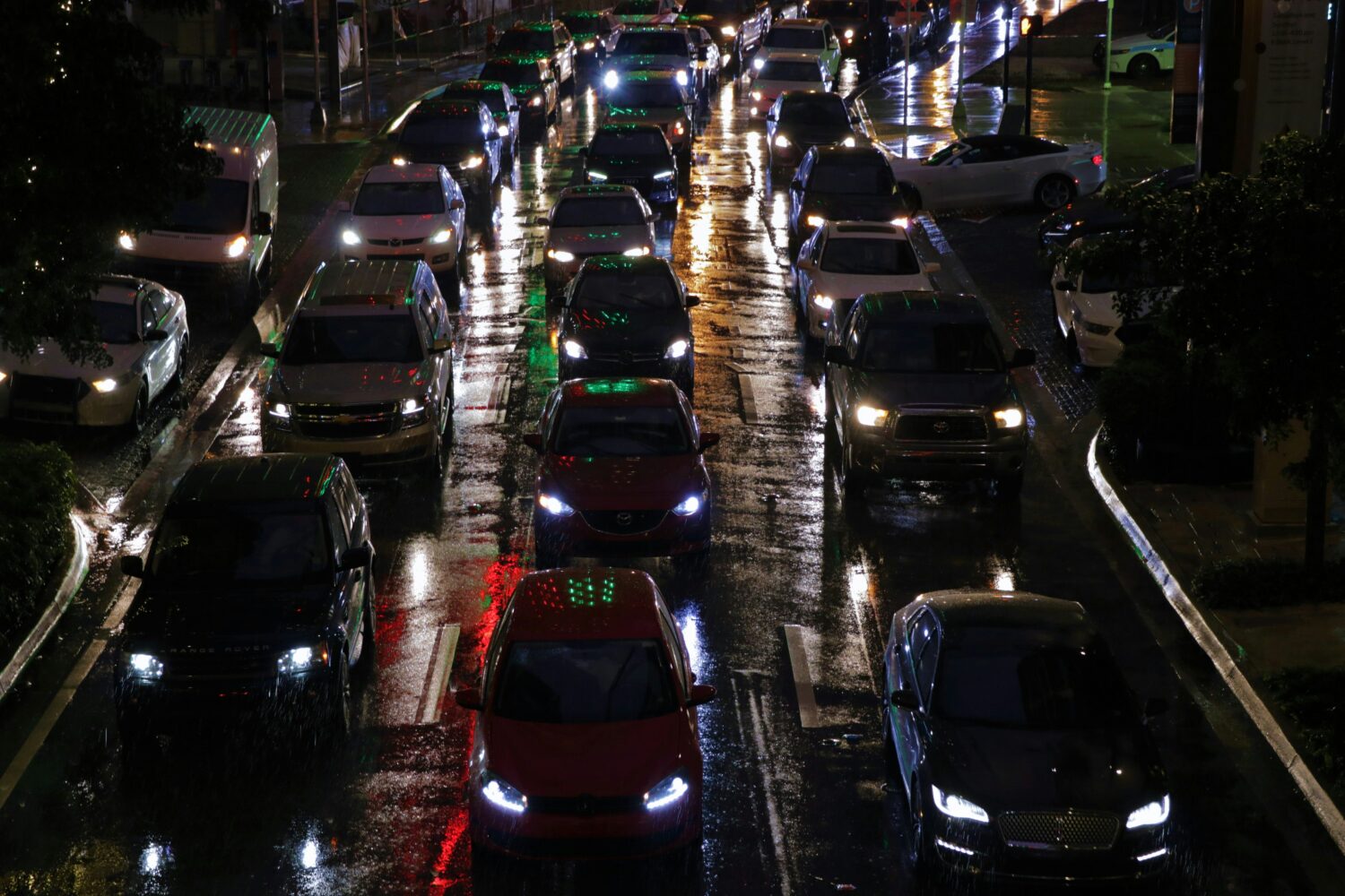 Tæt trafik på en regnvåd vej om aftenen med reflekser fra billygter i asfalten. JAC Kloakservice hjælper med at håndtere regnvand og forebygge oversvømmelser, der kan påvirke veje og byområder.